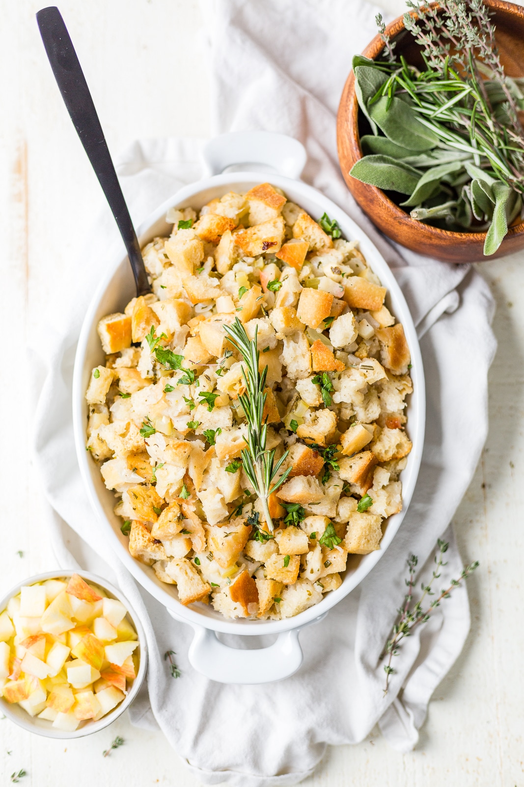 sourdough stuffing in a white casserole dish with a serving spoon and fresh herbs