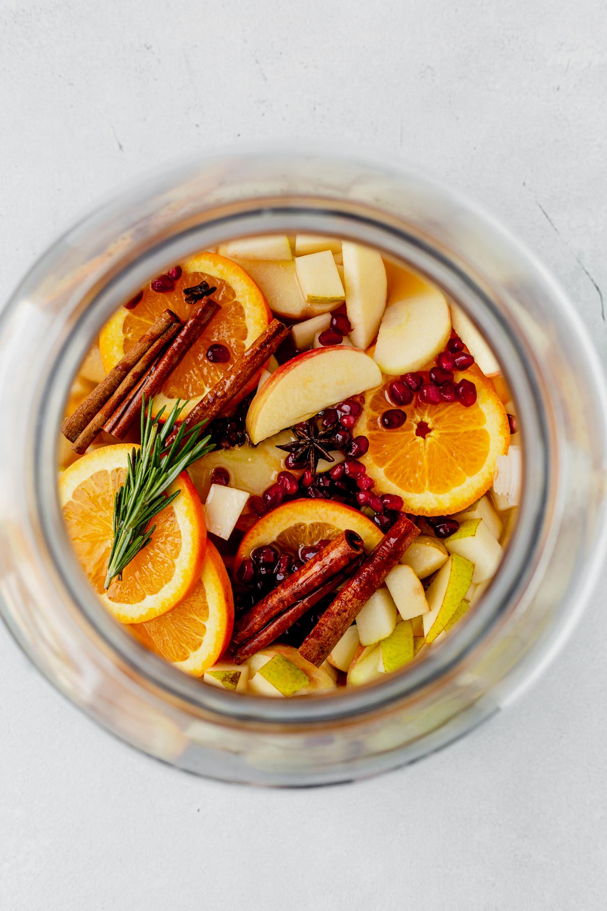 oranges, cinnamone sticks, rosemary and apples in a pitcher