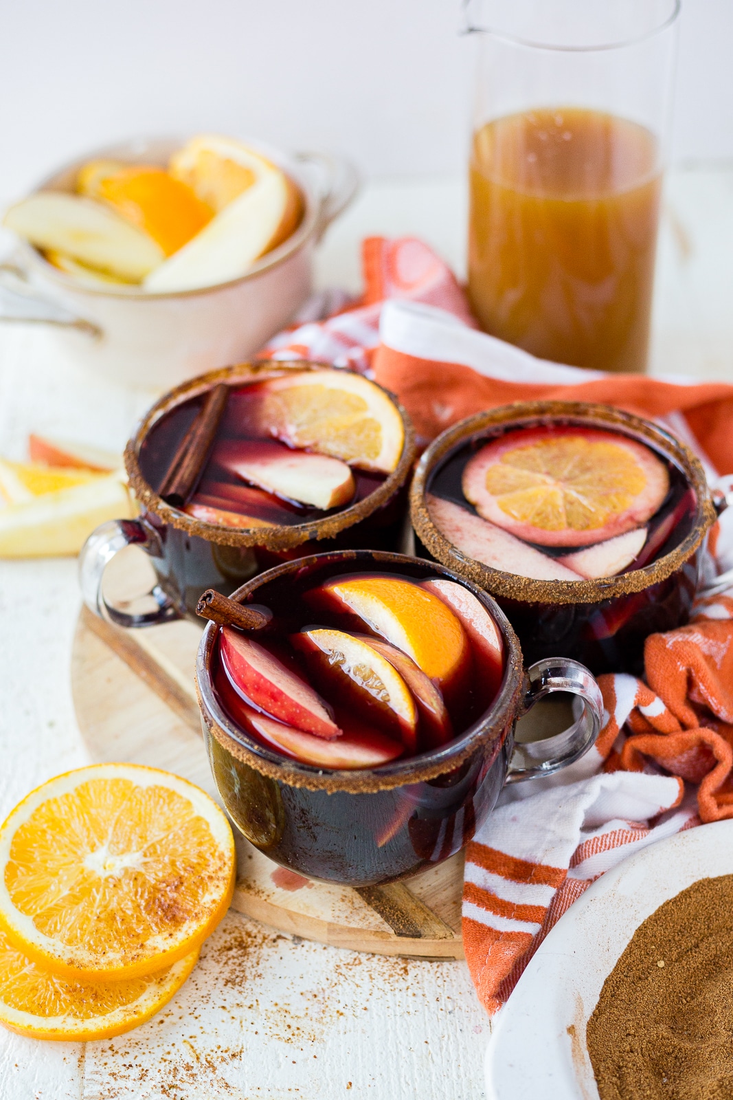 3 cups of winter sangria surrounded by apple cider and fresh frui