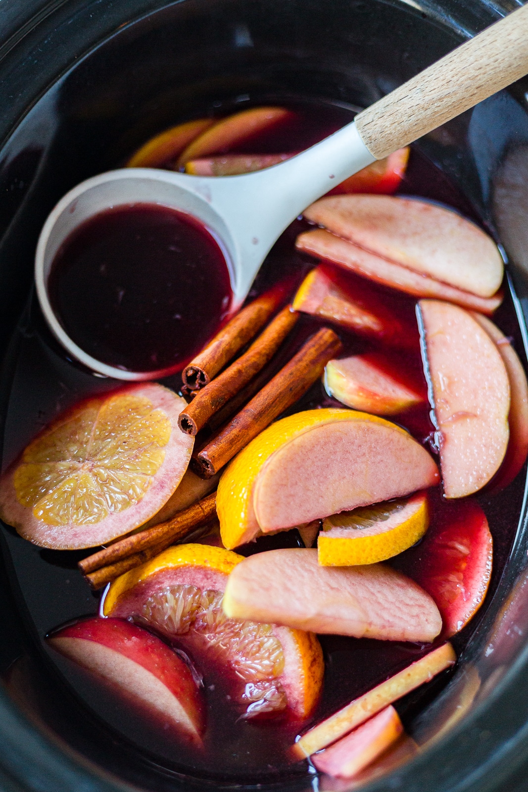 winter sangria recipe in a crock pot with sliced apples, oranges and cinnamon sticks