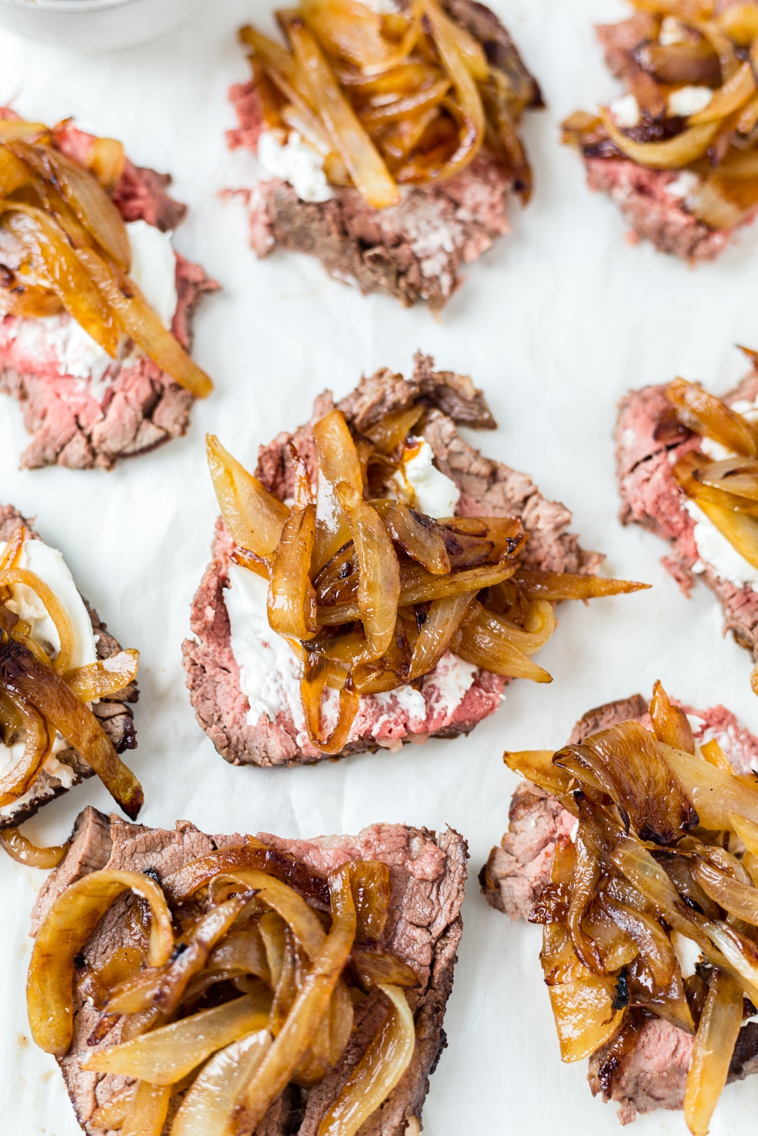 8 pieces of thinly sliced beef tenderloin on a cutting board topped with goat cheese and caramelized onion