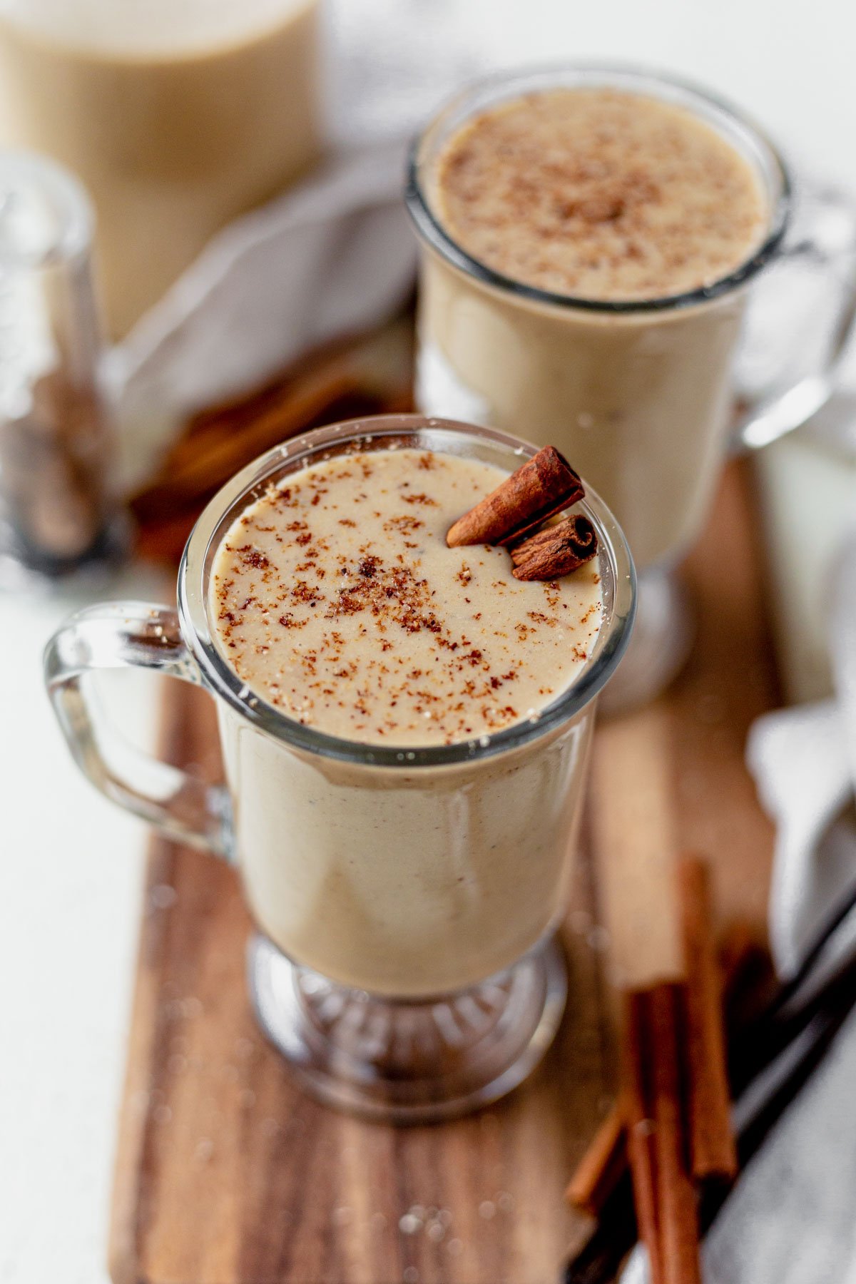 two glasses of dairy free eggnog garnished with nutmeg and cinnamon sticks