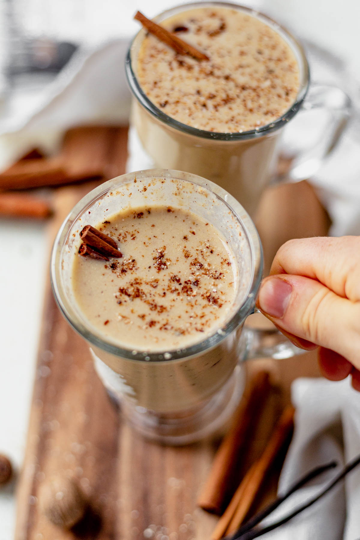 a hand holding half a glass of dairy free eggnog with fresh nutmeg