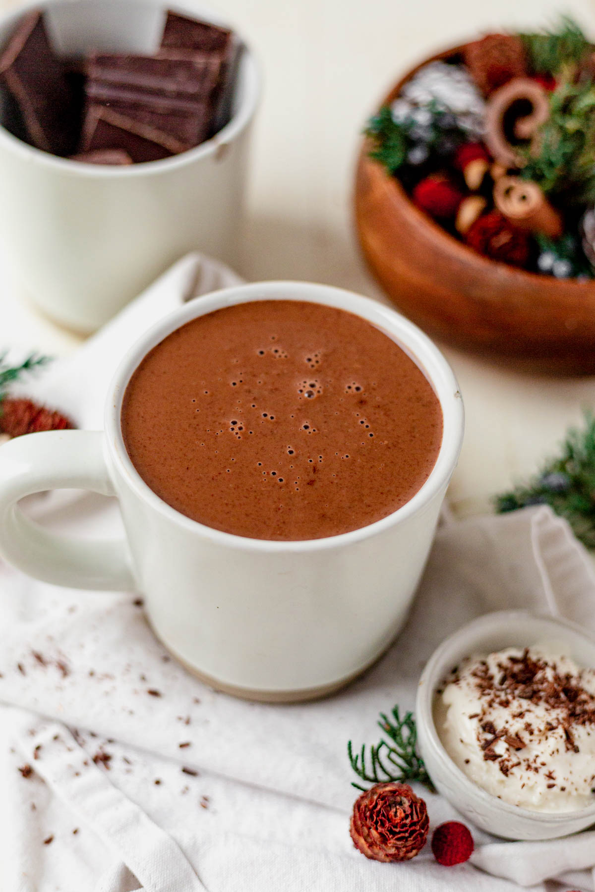 creamy dairy-free hot chocolate in a white mug next to holiday greenery and chopped chocolate