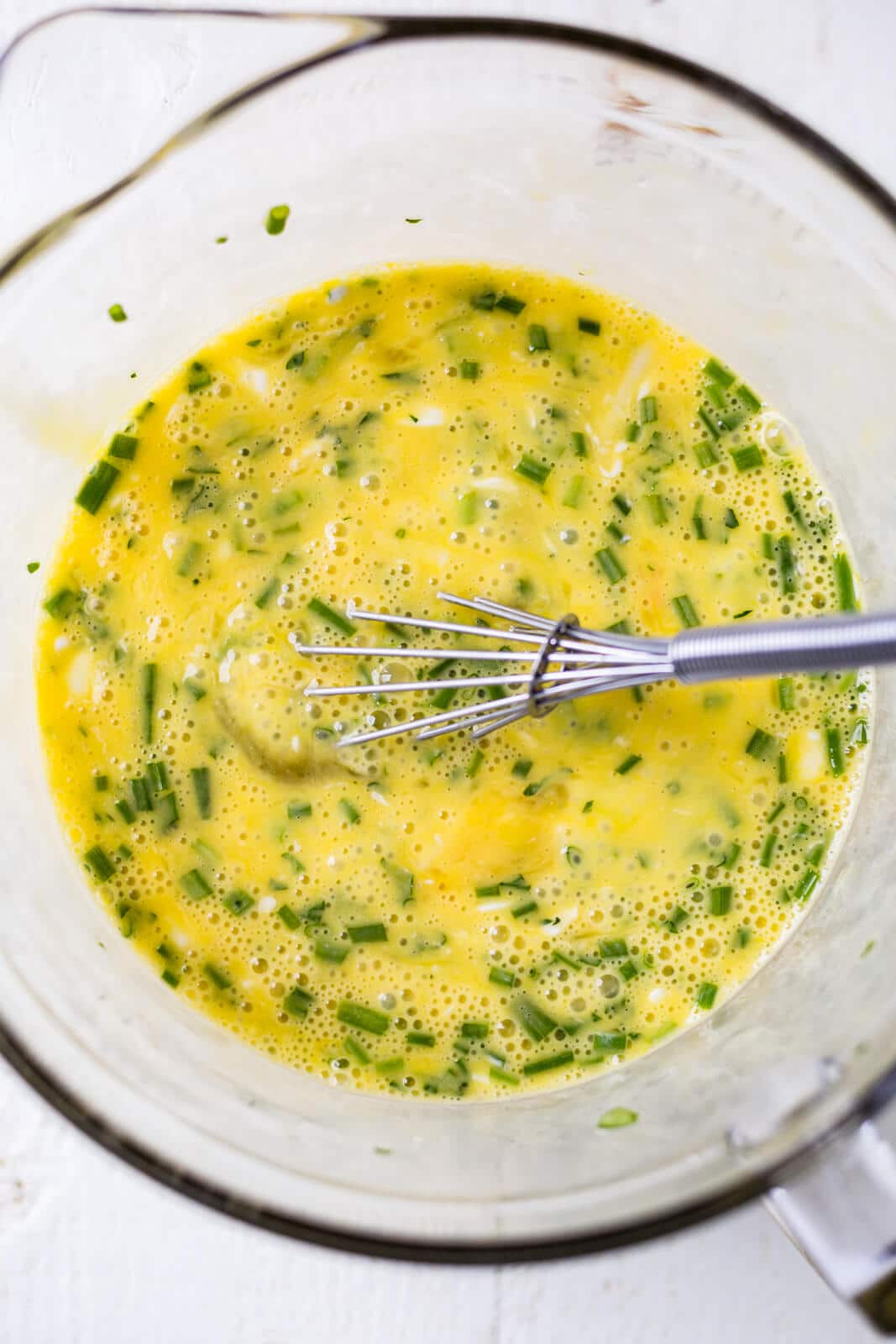 whisked eggs with cream and fresh herbs in a glass measuring bowl