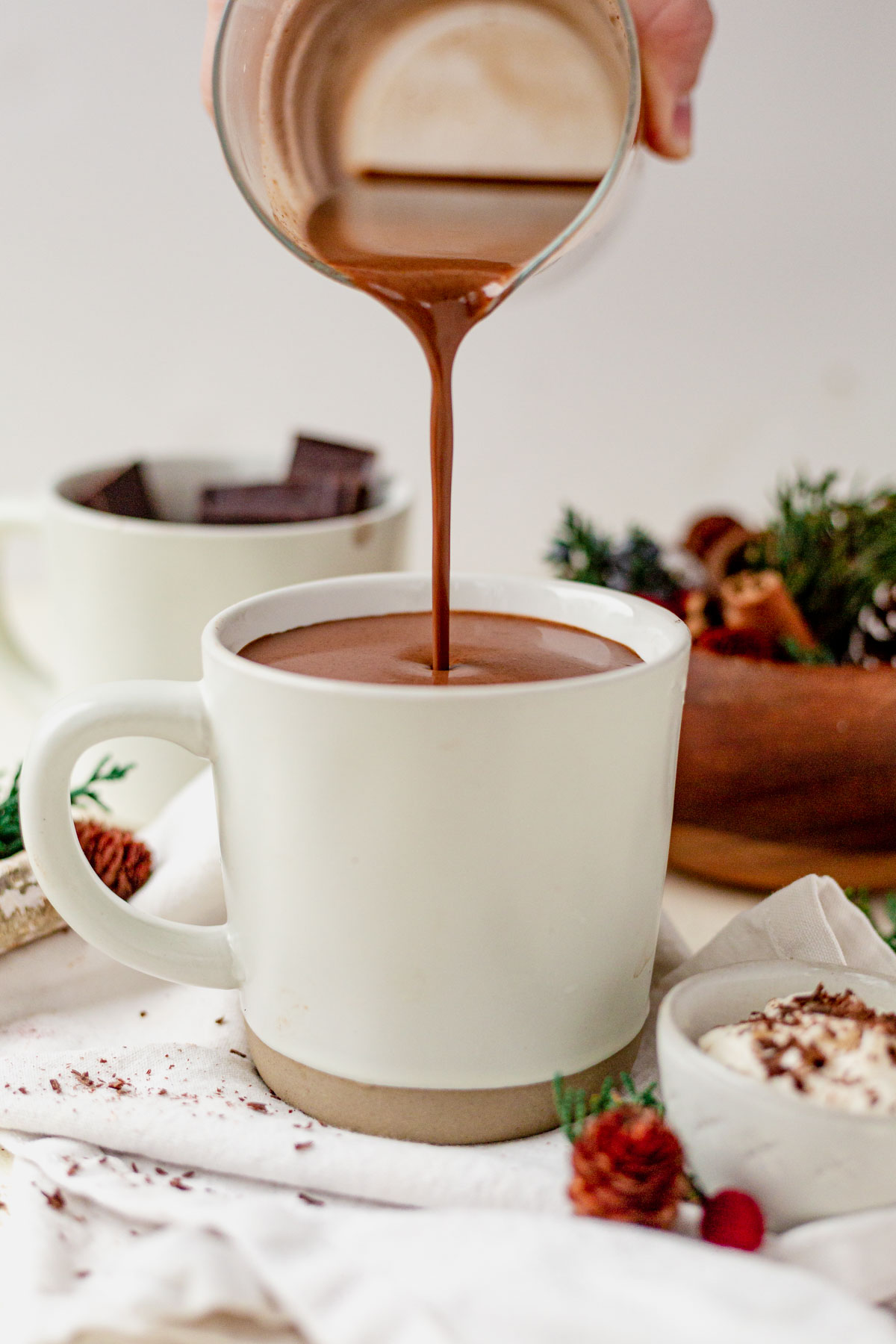 a hand pouring homemade dairy free hot chocolate into a white mug