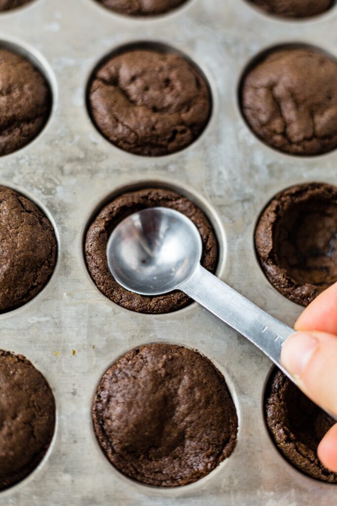 the back of a teaspoon pressing a hole into baked hot cocoa cookies in a muffin tin