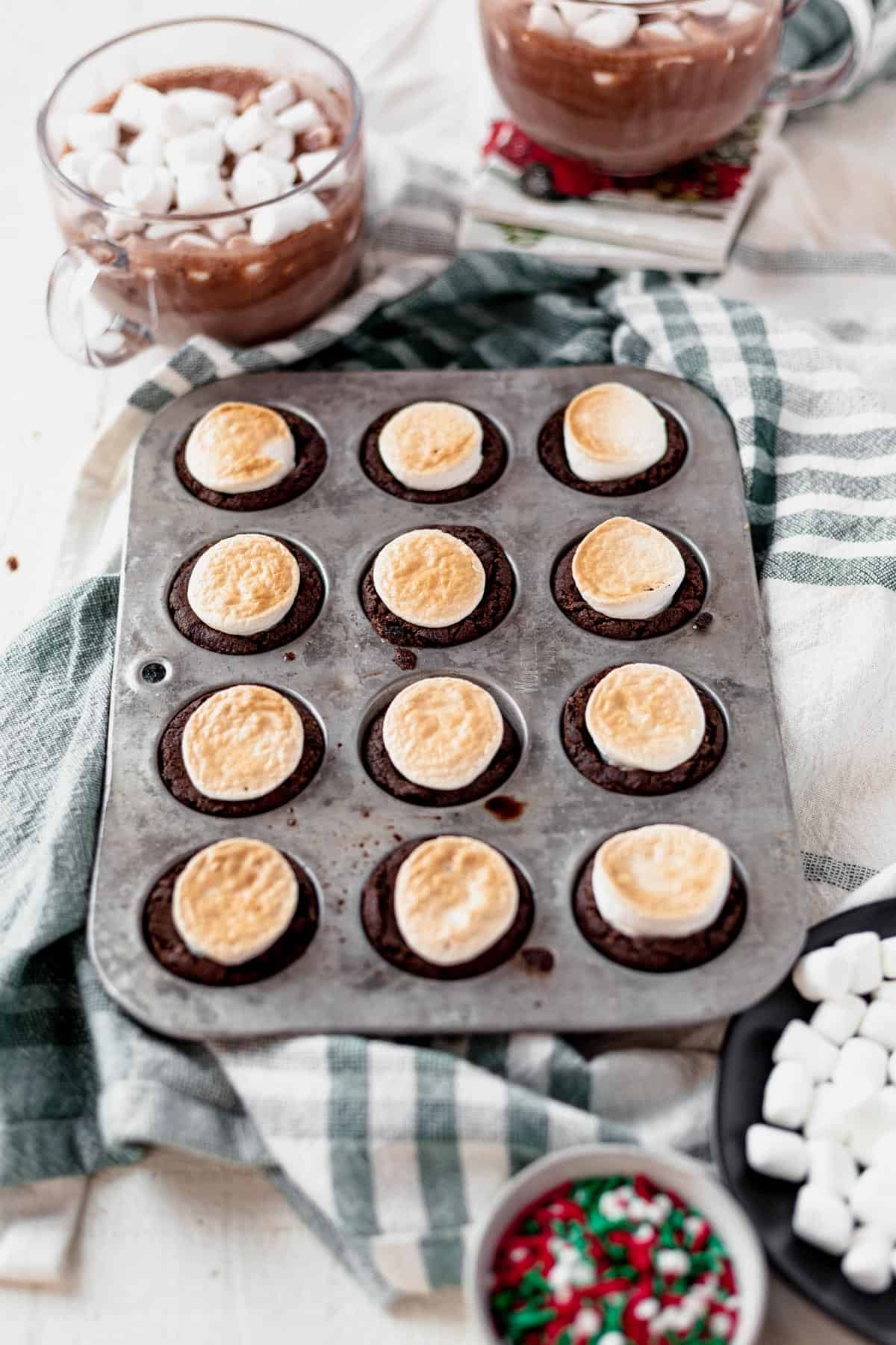 hot cocoa cookie cups in a muffin tin with toasted marshmallows
