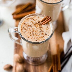 dairy free eggnog in a glass with fresh ground nutmeg and cinnamon sticks