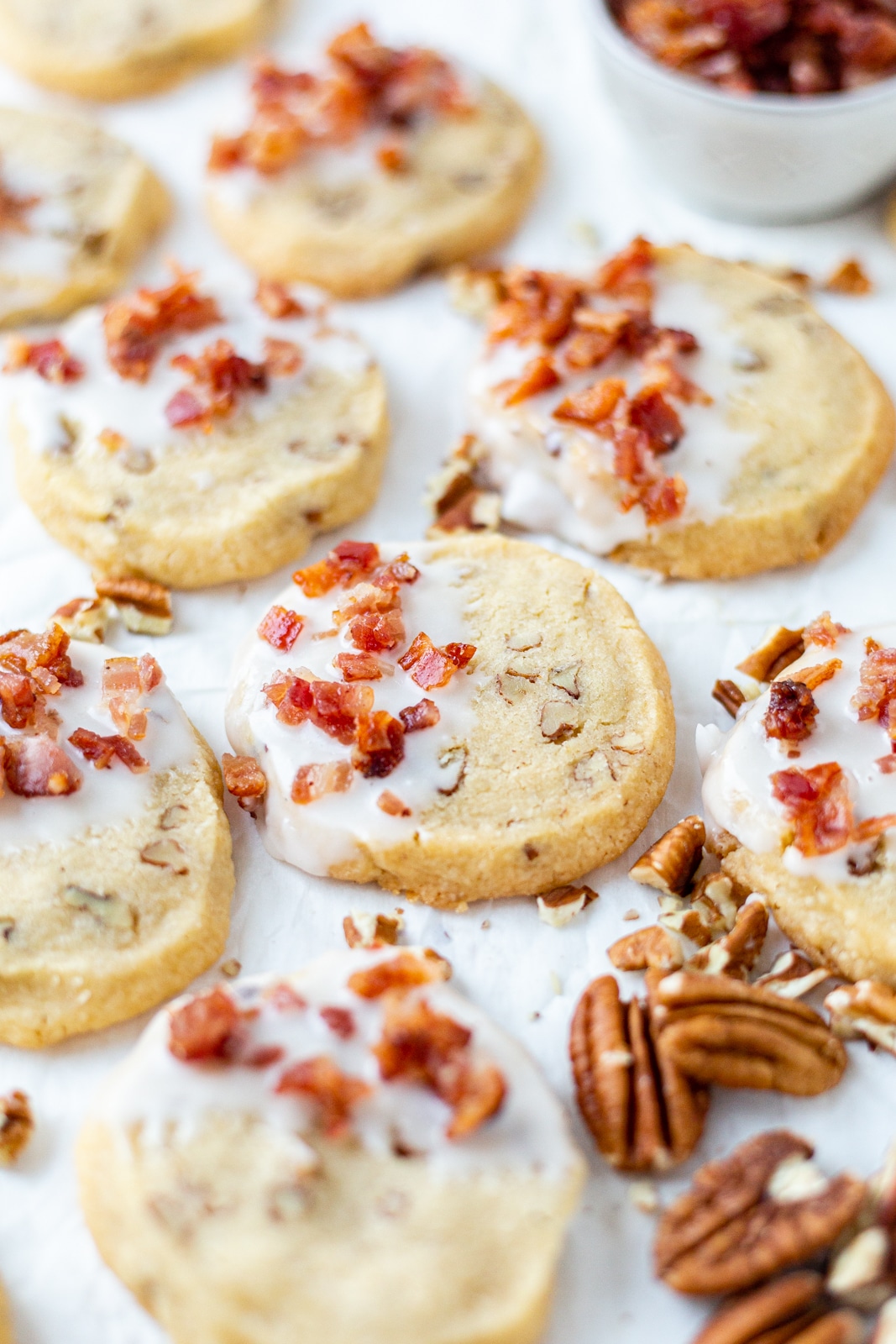 shortbread cookies arranged on parchment paper and decorated with maple glaze and candied bacon