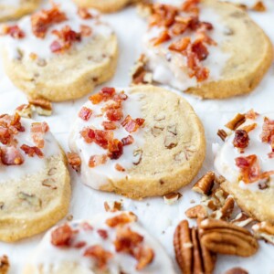 shortbread cookies arranged on parchment paper and decorated with maple glaze and candied bacon