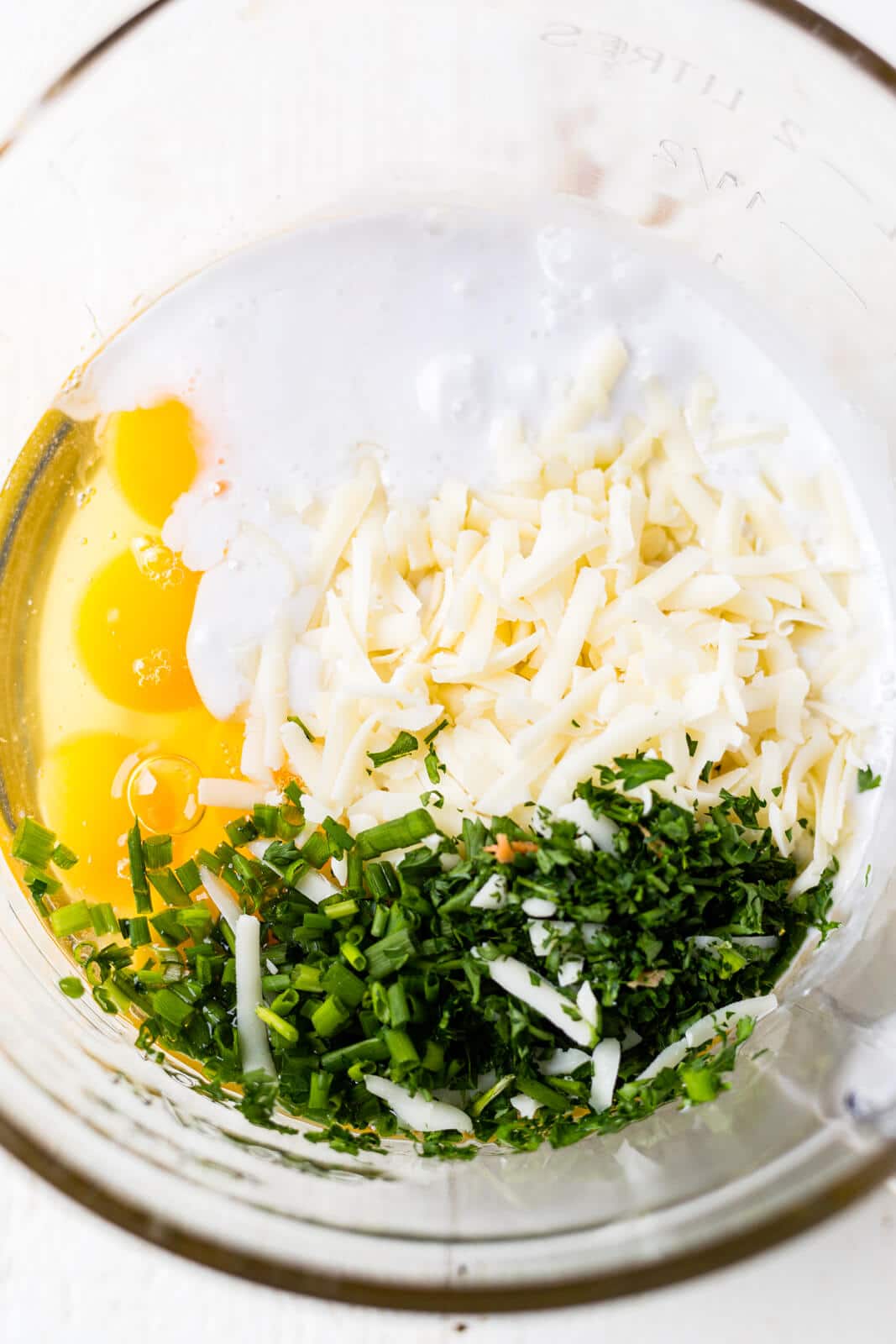 a glass measuring bowl filled with eggs, cream, cheese and herbs for frittata