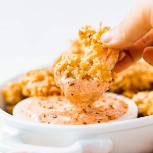 crispy golden brown air fryer shrimp being dipped into a spicy remoulade sauce