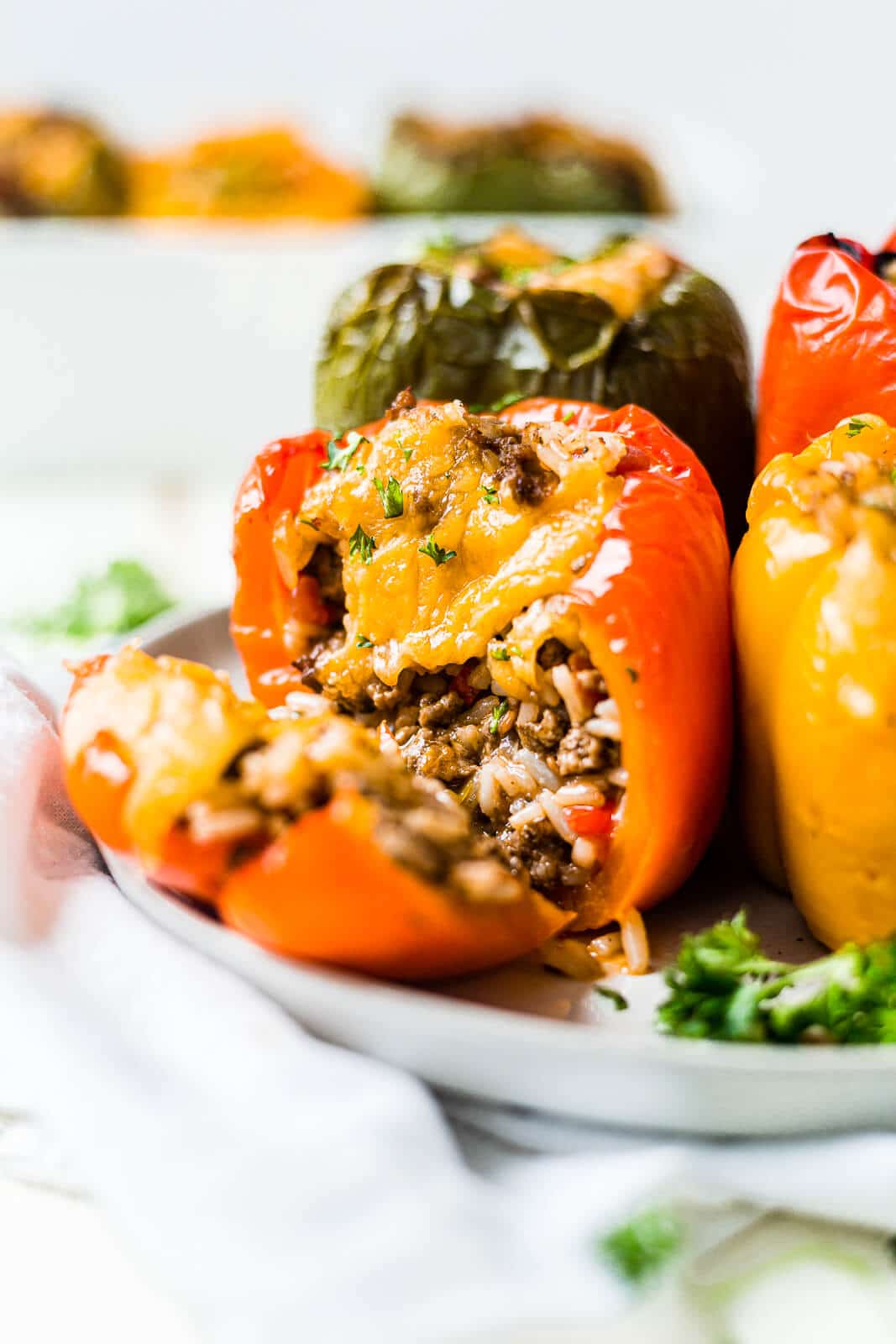 air fryer stuffed peppers in a white plate topped with cheese and parsley with one cut open to see the rice and beef inside