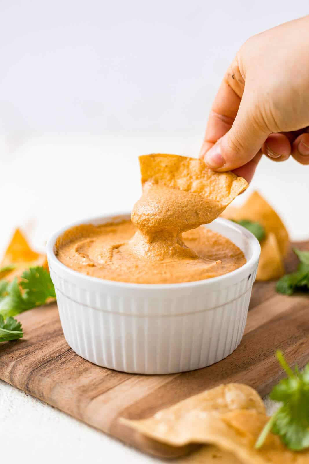 a hand dipping a chip into creamy cashew queso and pulling the chip out 