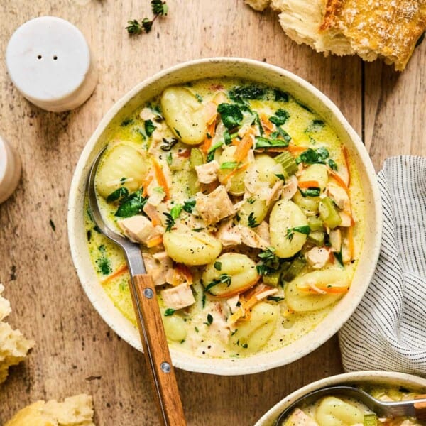 a bowl of chicken gnocchi soup on a table with crusty bread on the side.