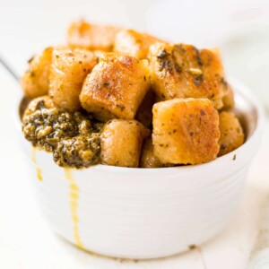 crispy cauliflower gnocchi in a white dish tossed with fresh basil pesto