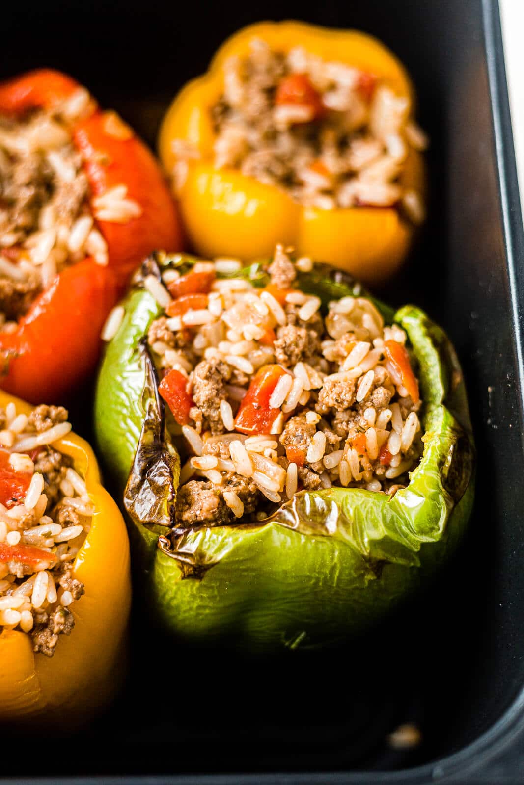 air fryer stuffed peppers in the basket with charred edges right before being topped with cheese