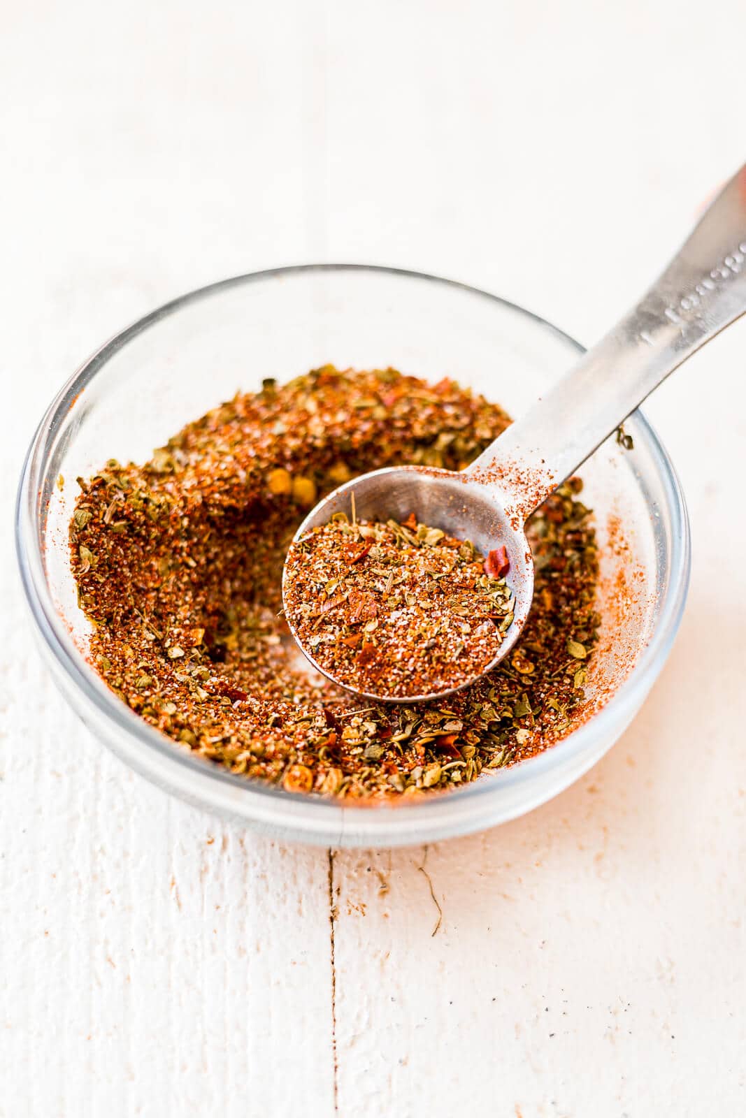 cajun seasoning in a small glass bowl with a teaspoon being scooped out onto shrimp pasta