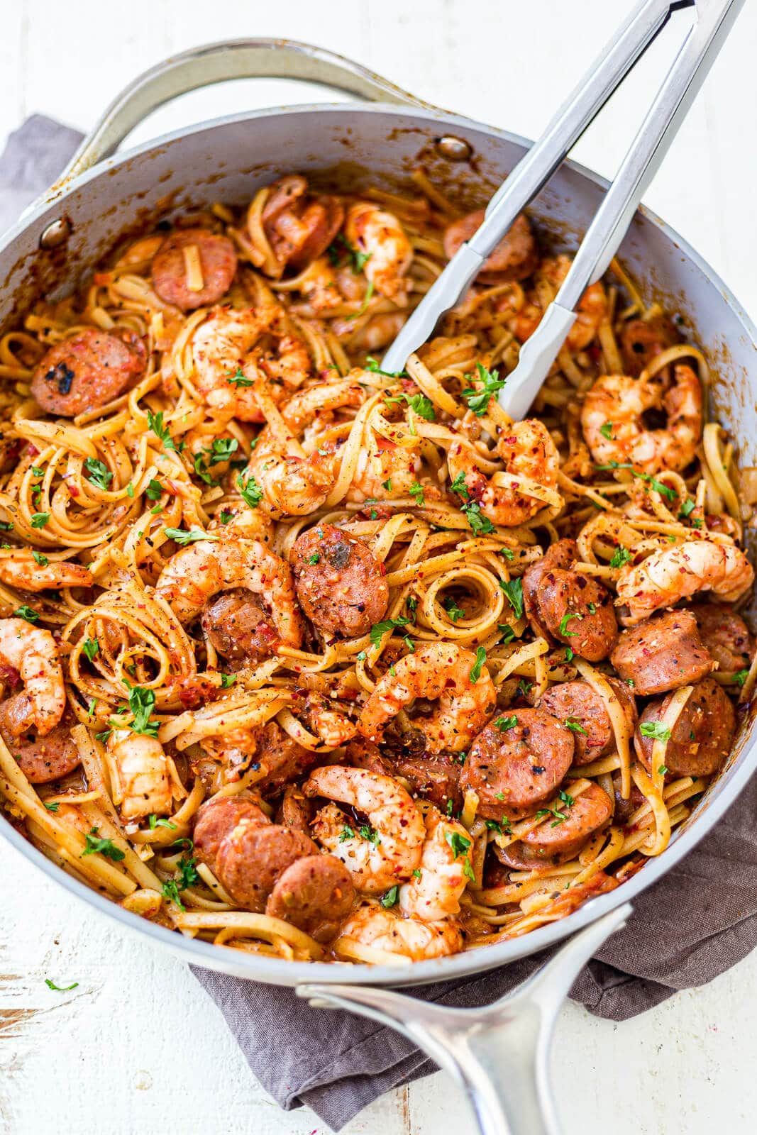 one pot creamy cajun shrimp pasta in a deep skillet topped with fresh parsley and a set of grey tongs scooping some pasta out
