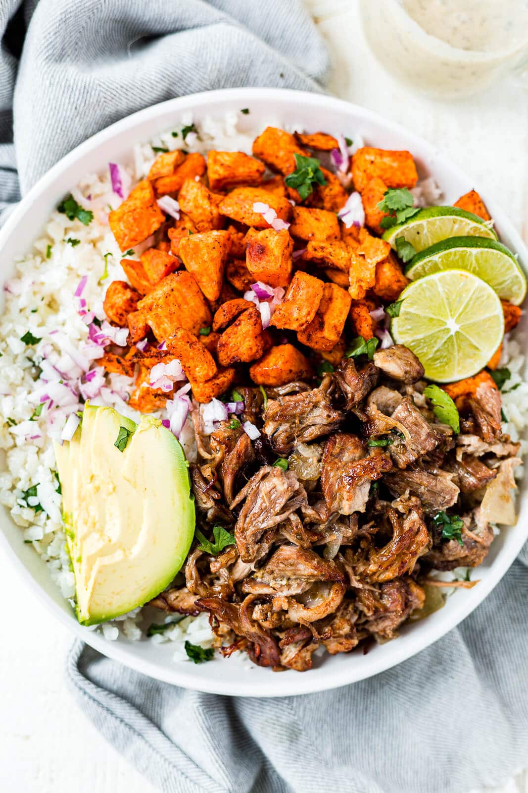 instant pot carnitas in a burrito bowl with sweet potatoes, rice, onion, lime and avocado