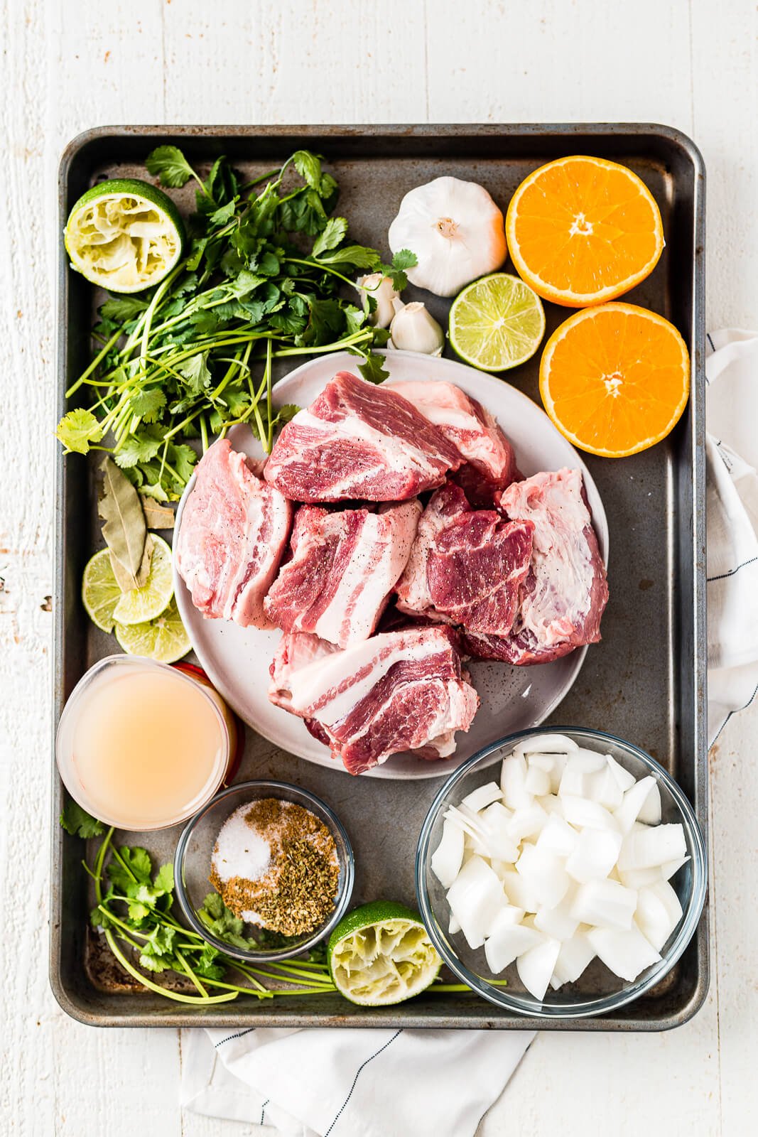 a large sheet pan with all of the ingredients for instant pot pork carnitas including pork shoulder, onion, oranges, limes, spices and garlic
