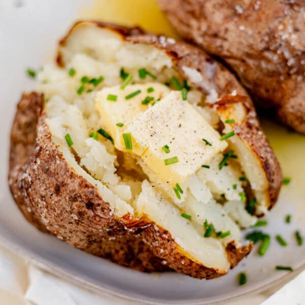 air fryer baked potato on a plate with butter and chives.