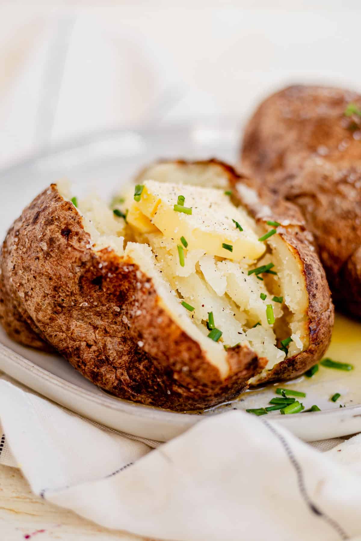 a crispy air fryer baked potato on a plate with butter and chives.