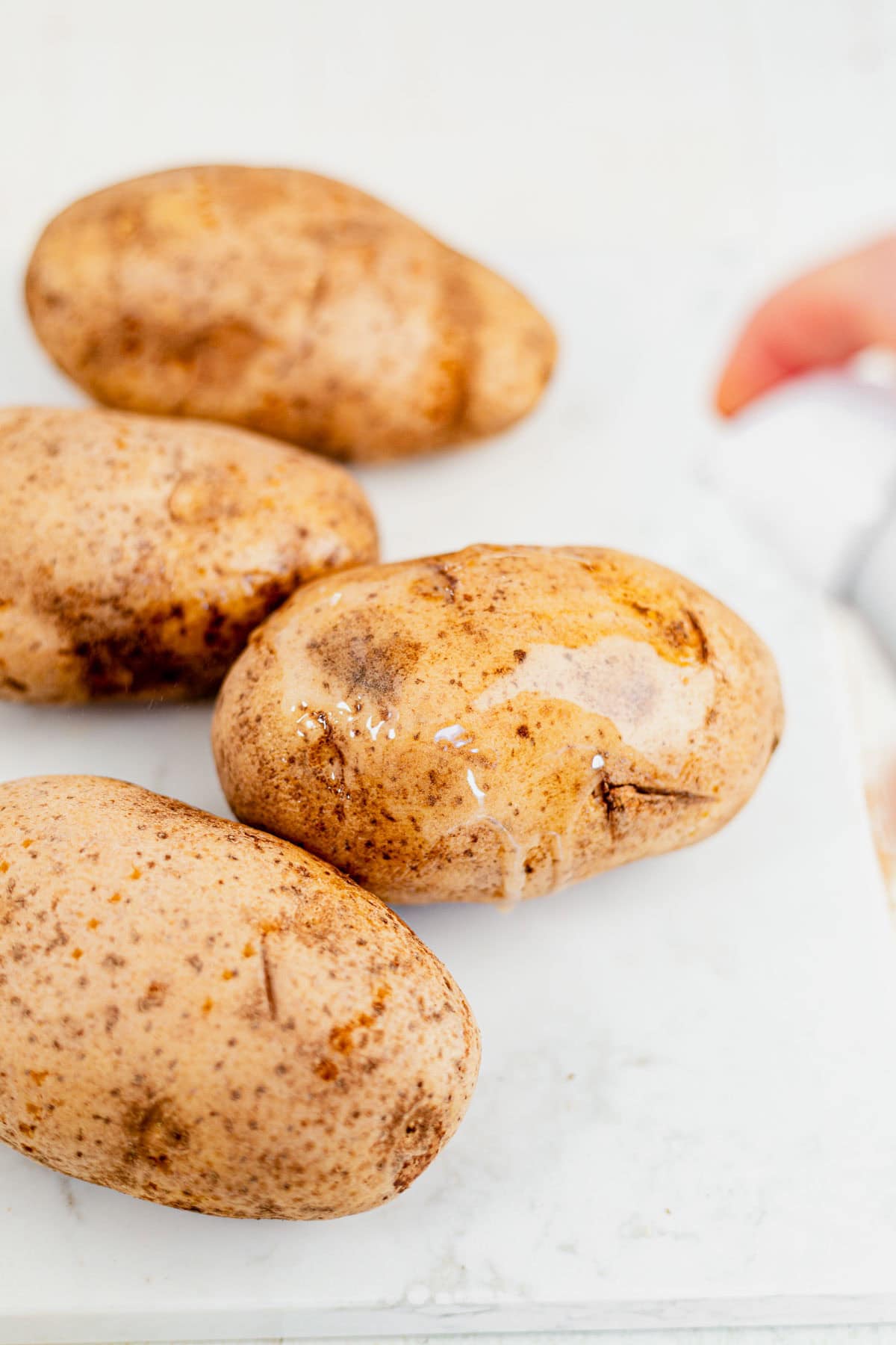 4 russet potatoes on a counter sprayed with cooking spray.