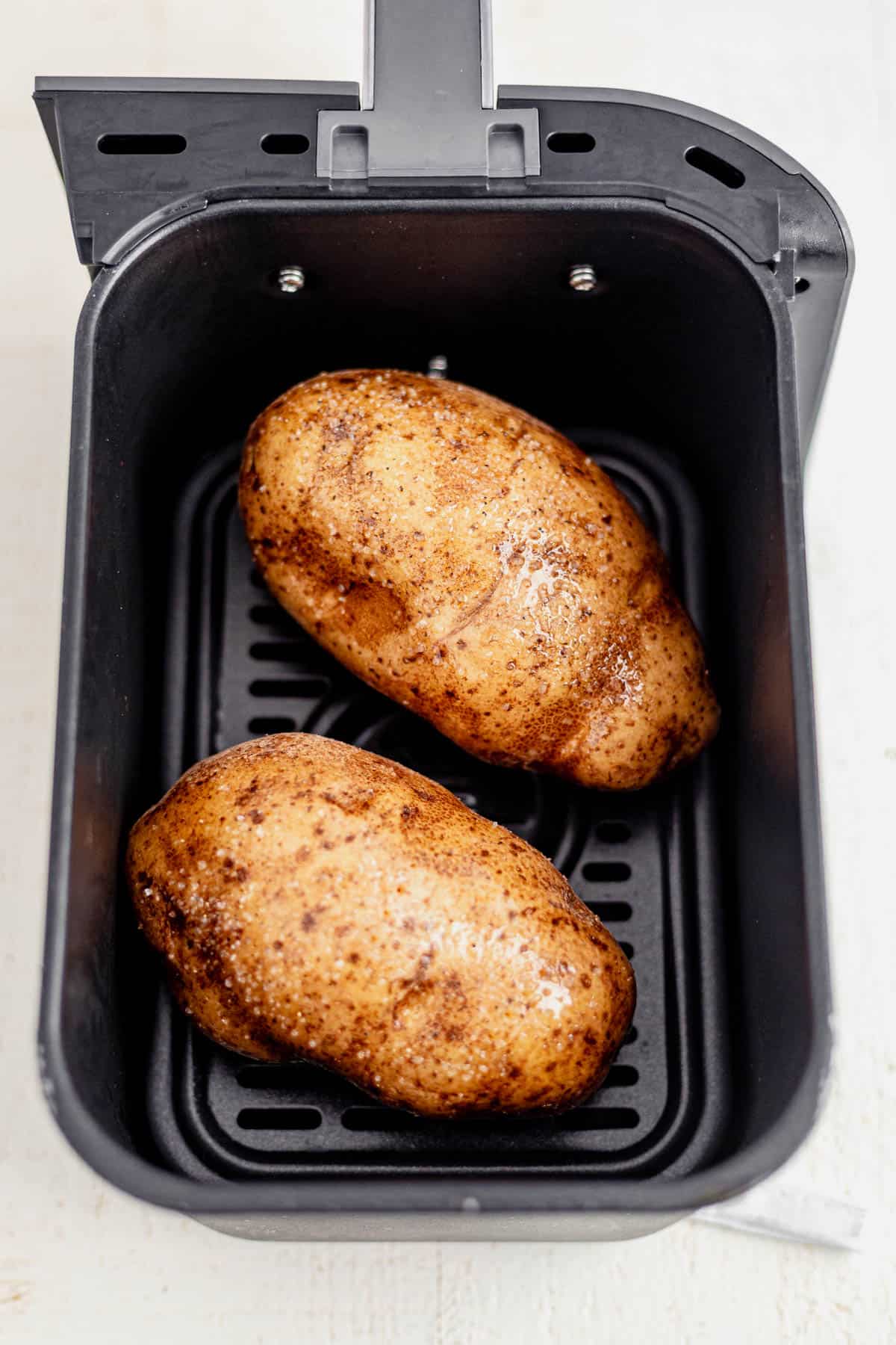 two russet potatoes in an air fryer basket.