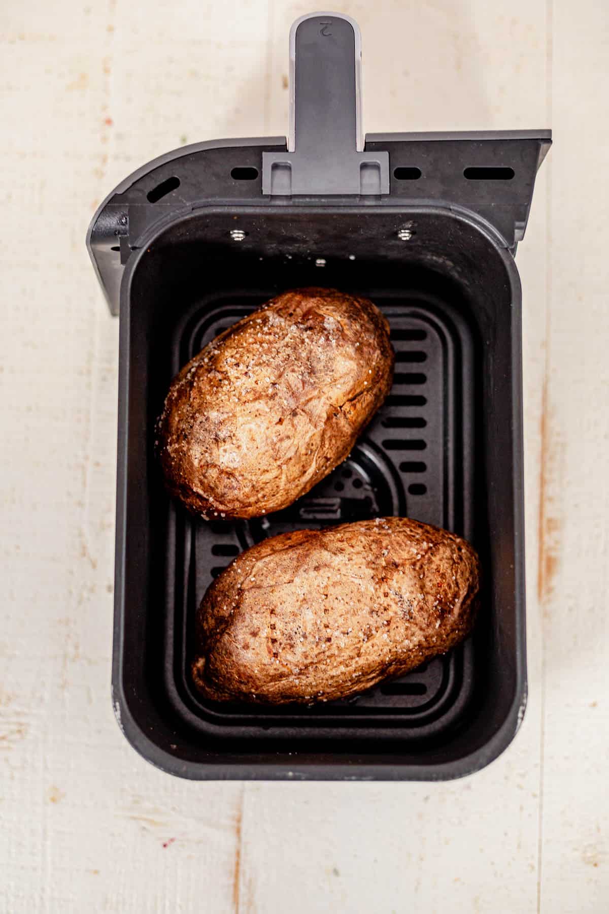 two air fryer baked potatoes in an air fryer basket.