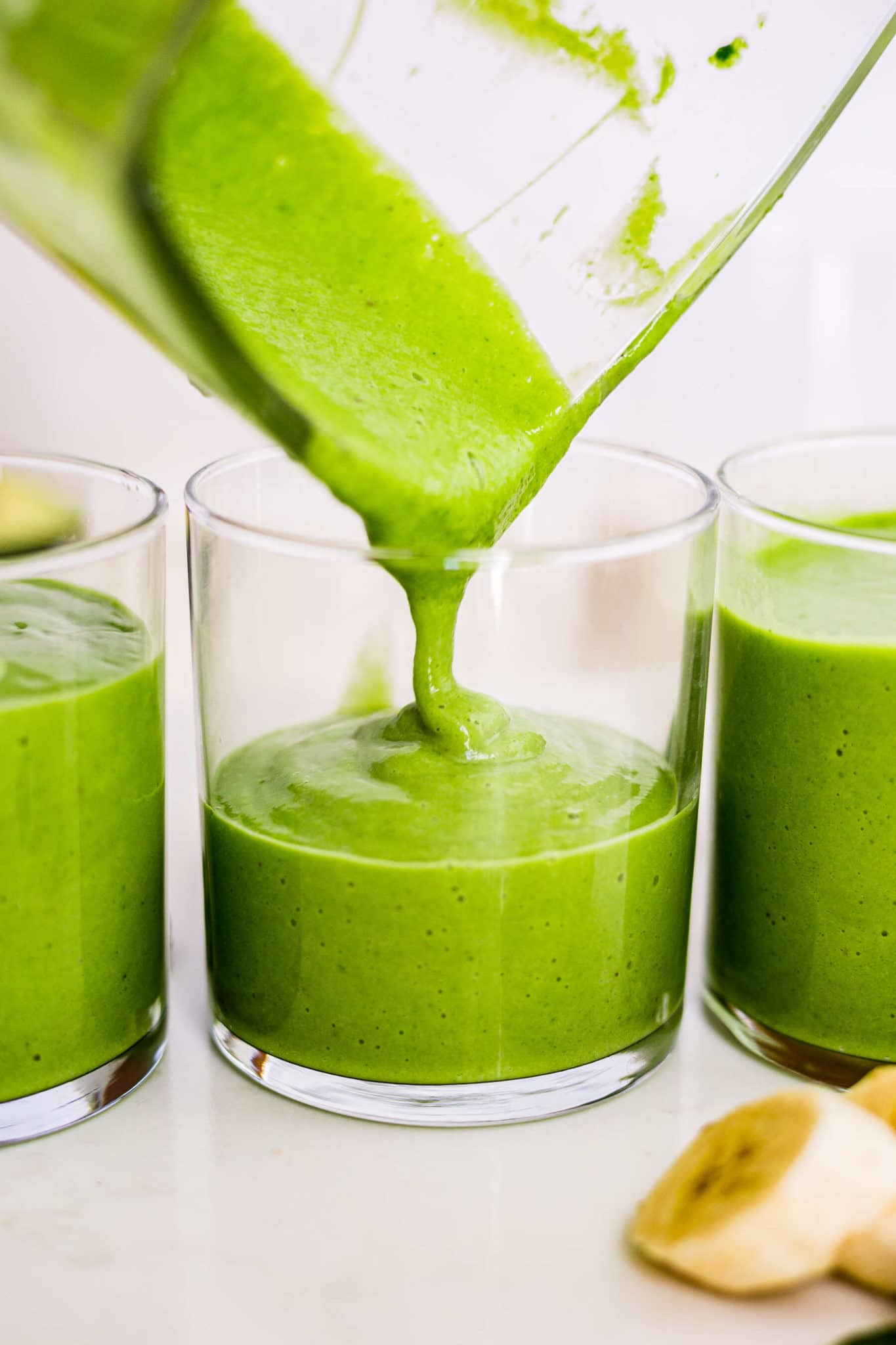 green avocado smoothie pouring into a short glass form the blender