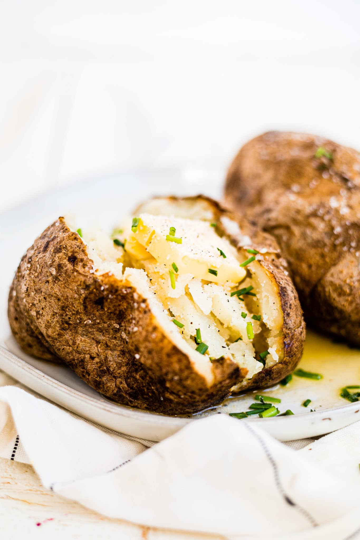 air fryer baked potato cut open and topped with butter and chives on a white plate