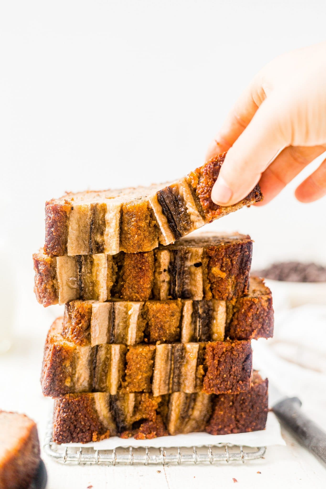 5 slices of banana bread made with almond flour stacked on top of each other with a hand reaching for the top one