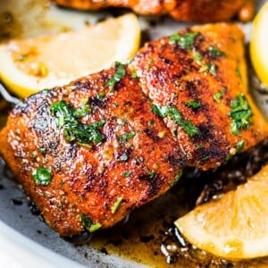 blackened salmon in a skillet with avocado oil and lemon and topped with fresh parsley