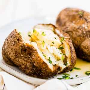 air fryer baked potato on a white plate cut open with butter and chives