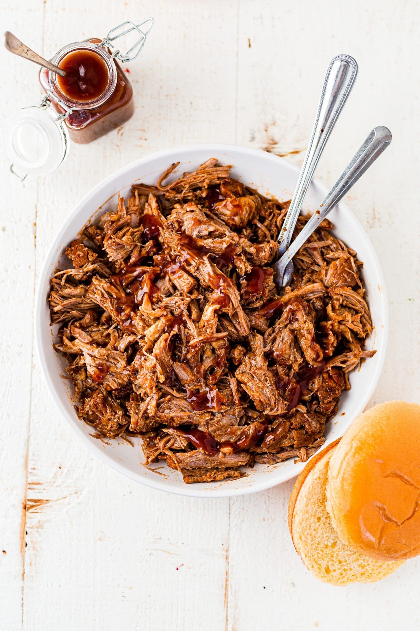 instant pot pulled pork tossed in bbq sauce in a large white bowl with 2 serving spoons