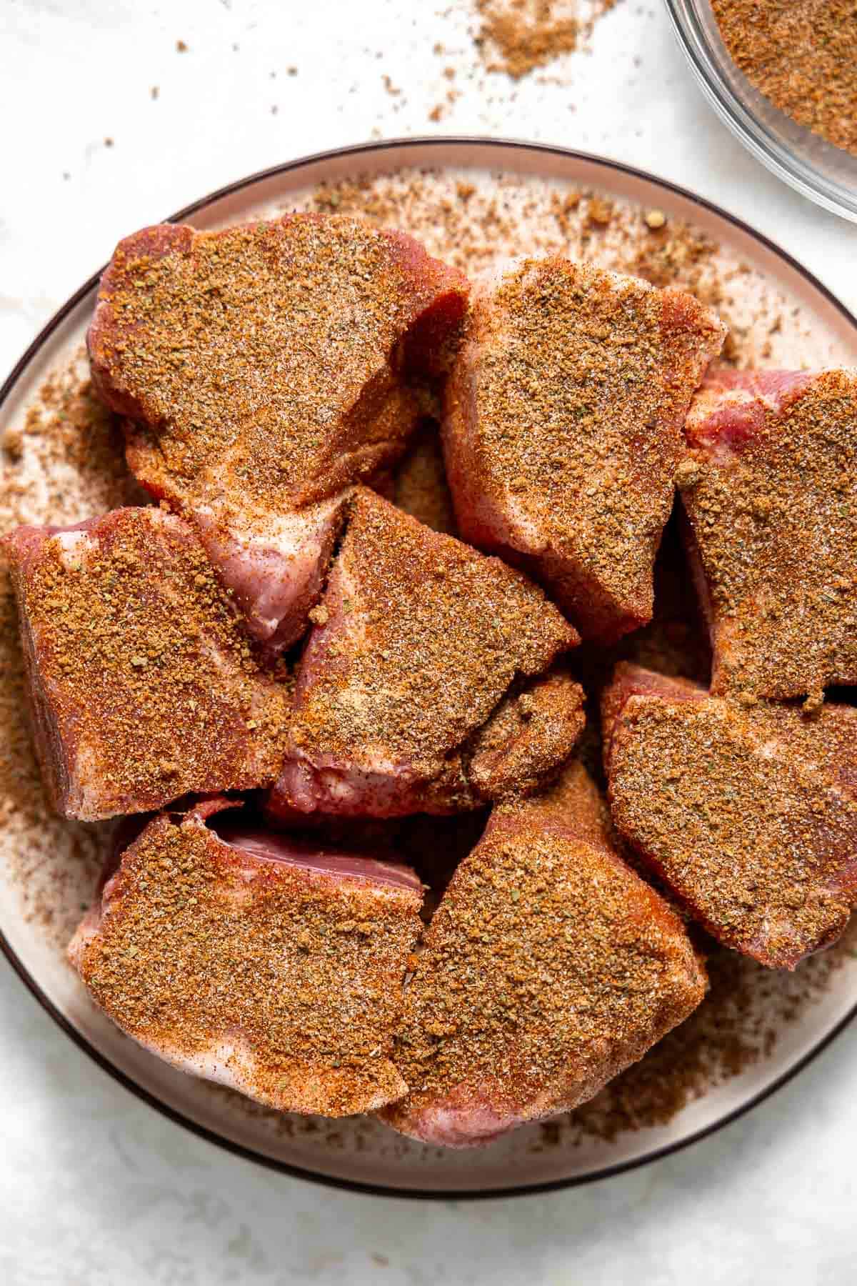 pieces of pork shoulder on a plate coated in dry rub.