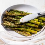 a pound of air fryer asparagus in a white serving dish with tongs for serving