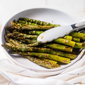 a pound of air fryer asparagus in a white serving dish with tongs for serving