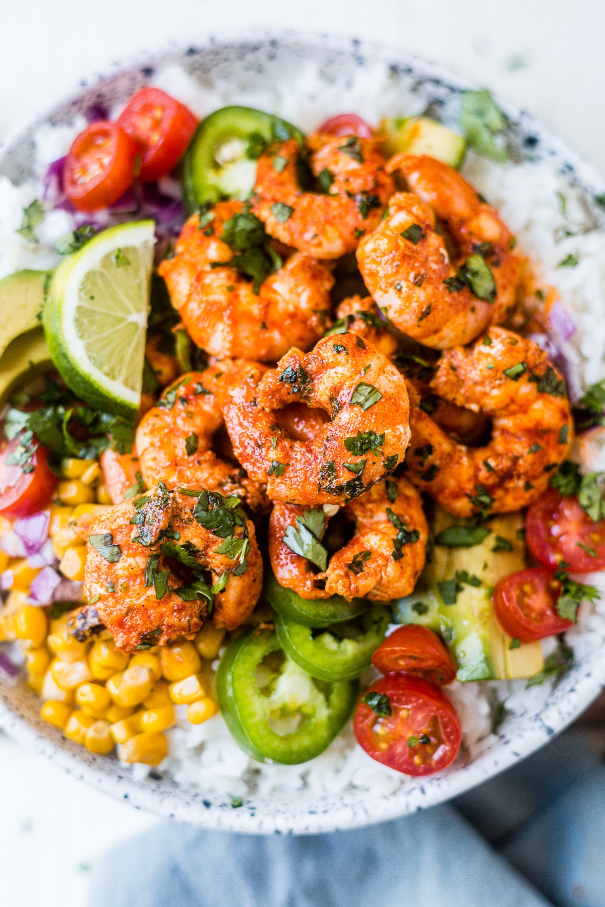 close up of fiest lime shrimp on a rice bowl with corn, avocado, jalapeno, tomato and fresh cilantro