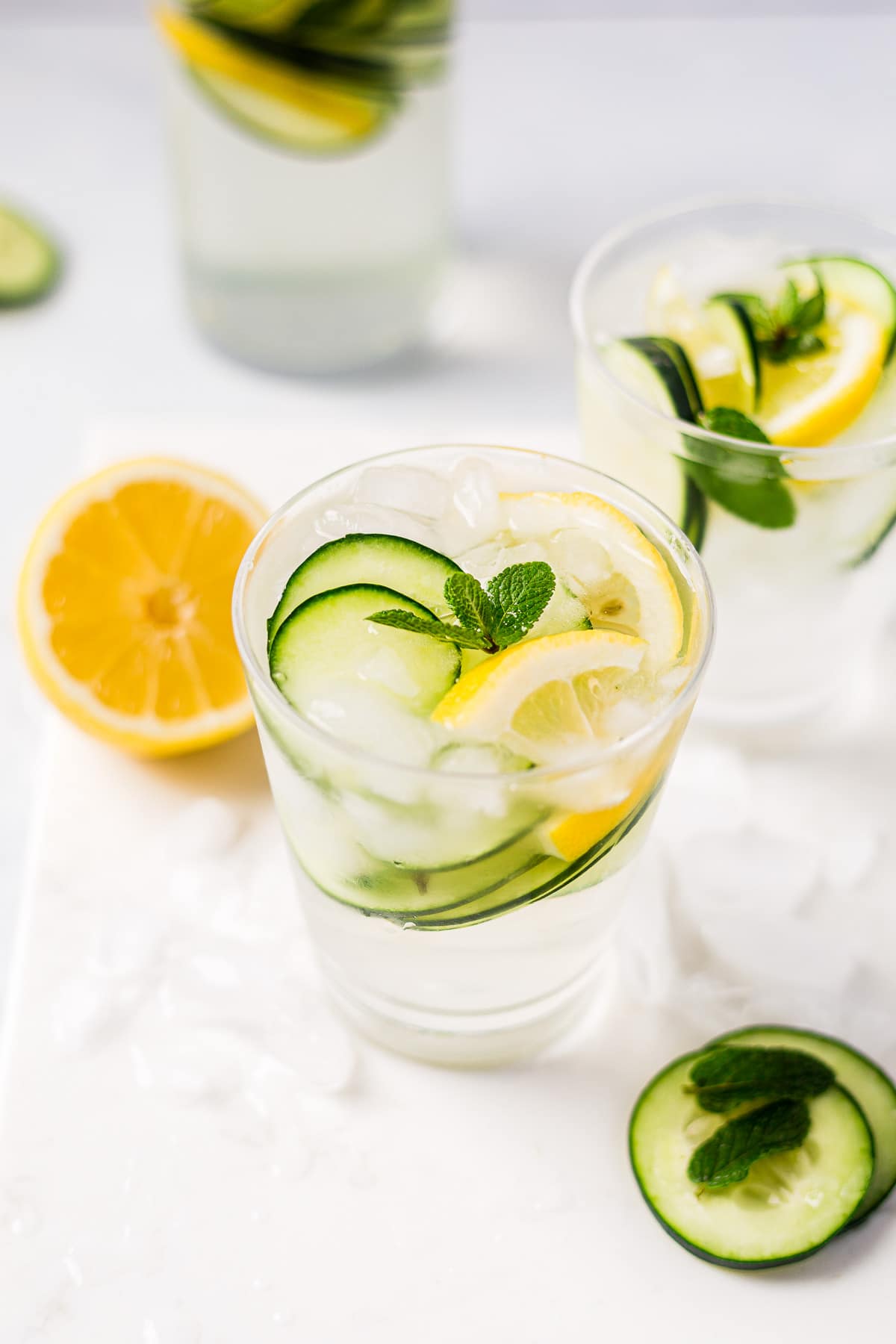 cucumber and lemon water in two cups with both topped with crushed ice and fresh mint