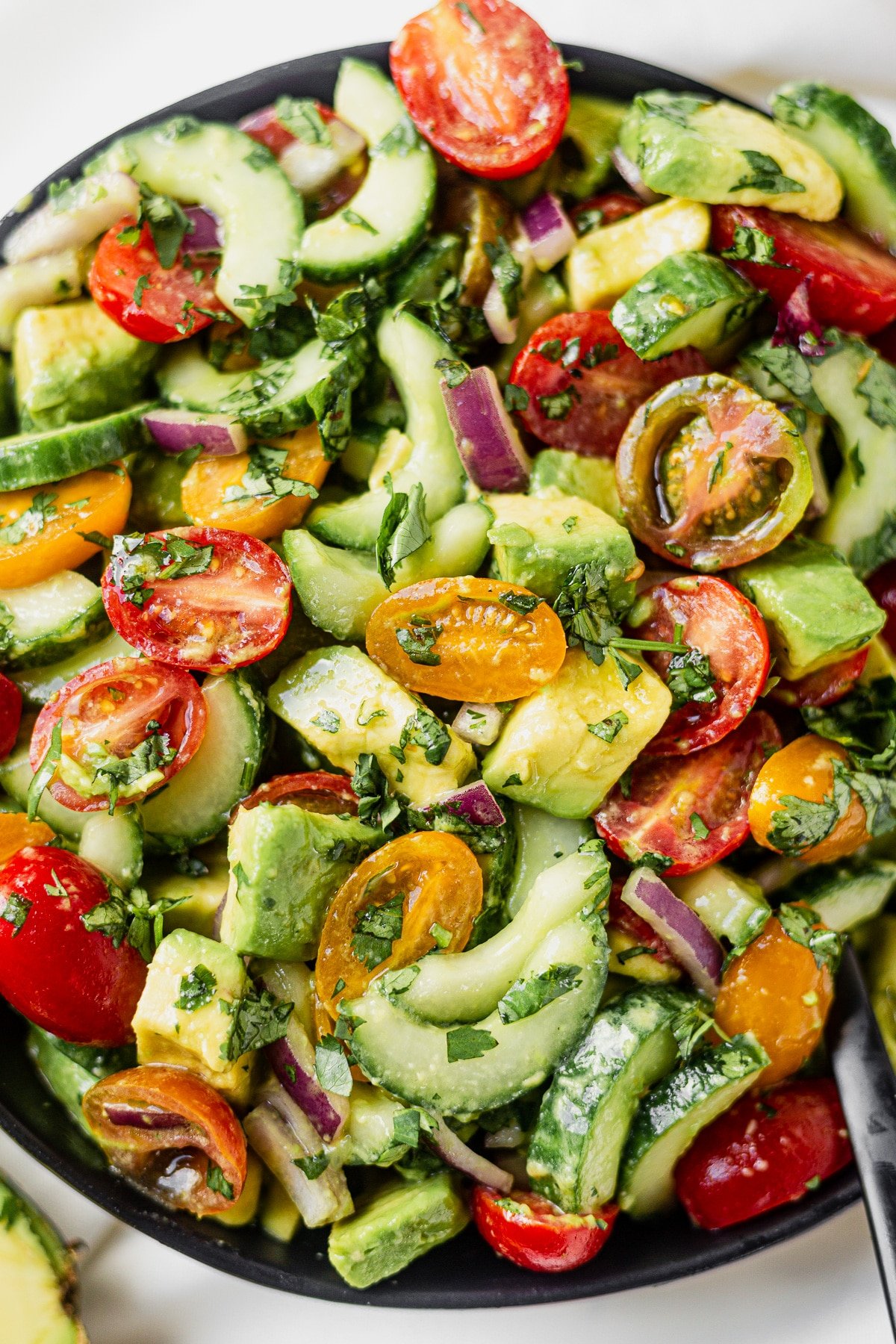 chopped avocado, sliced tomatoes and sliced avocado in a bowl with dressing and herbs