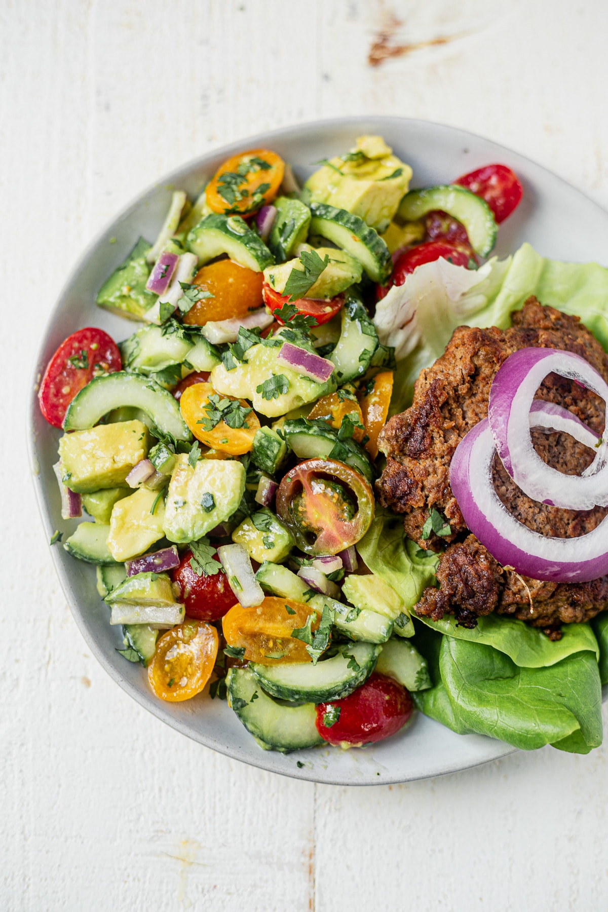 cucumber tomato avocado salad on a white plate with a burger