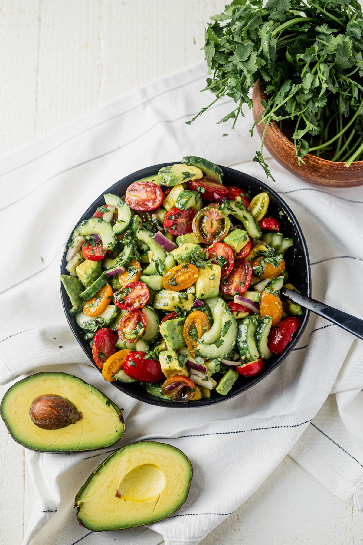 cucumber tomato avocado salad  in a black serving bowl with fresh avocado on the side