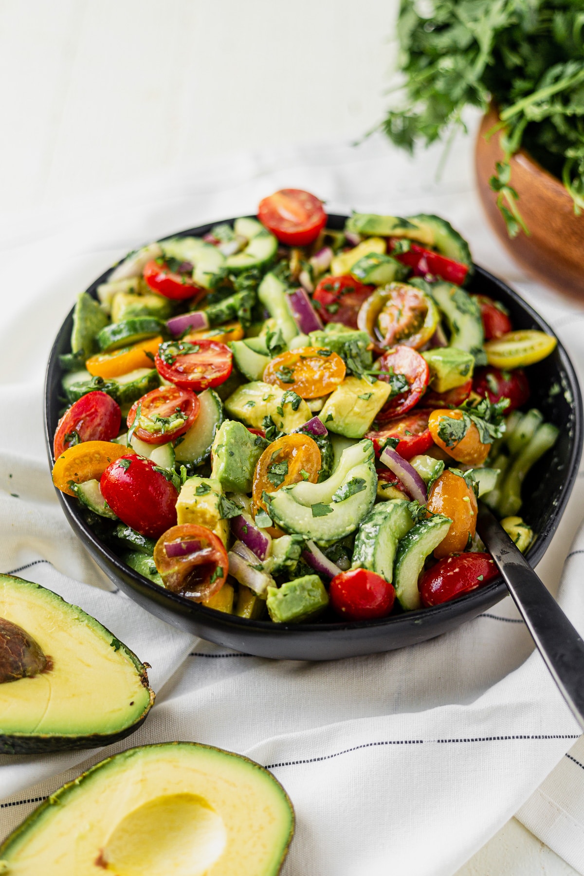 a large bowl of tomato cucumber avocado salad with a black serving spoon 