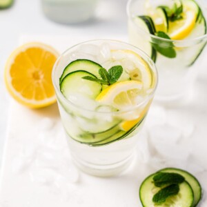 fresh cucumber water in a glass cup with lemon and a sprig of mint