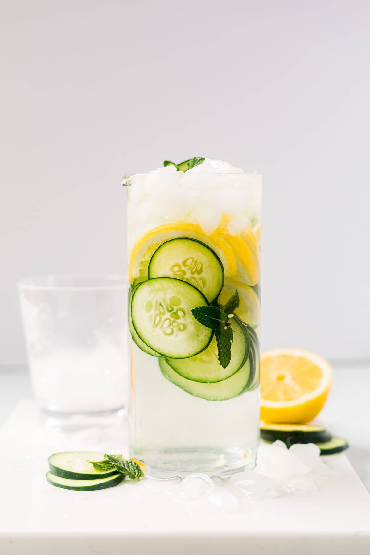 cucumber water in a pitcher with crushed ice, lemon and mint with cups for serving next to it