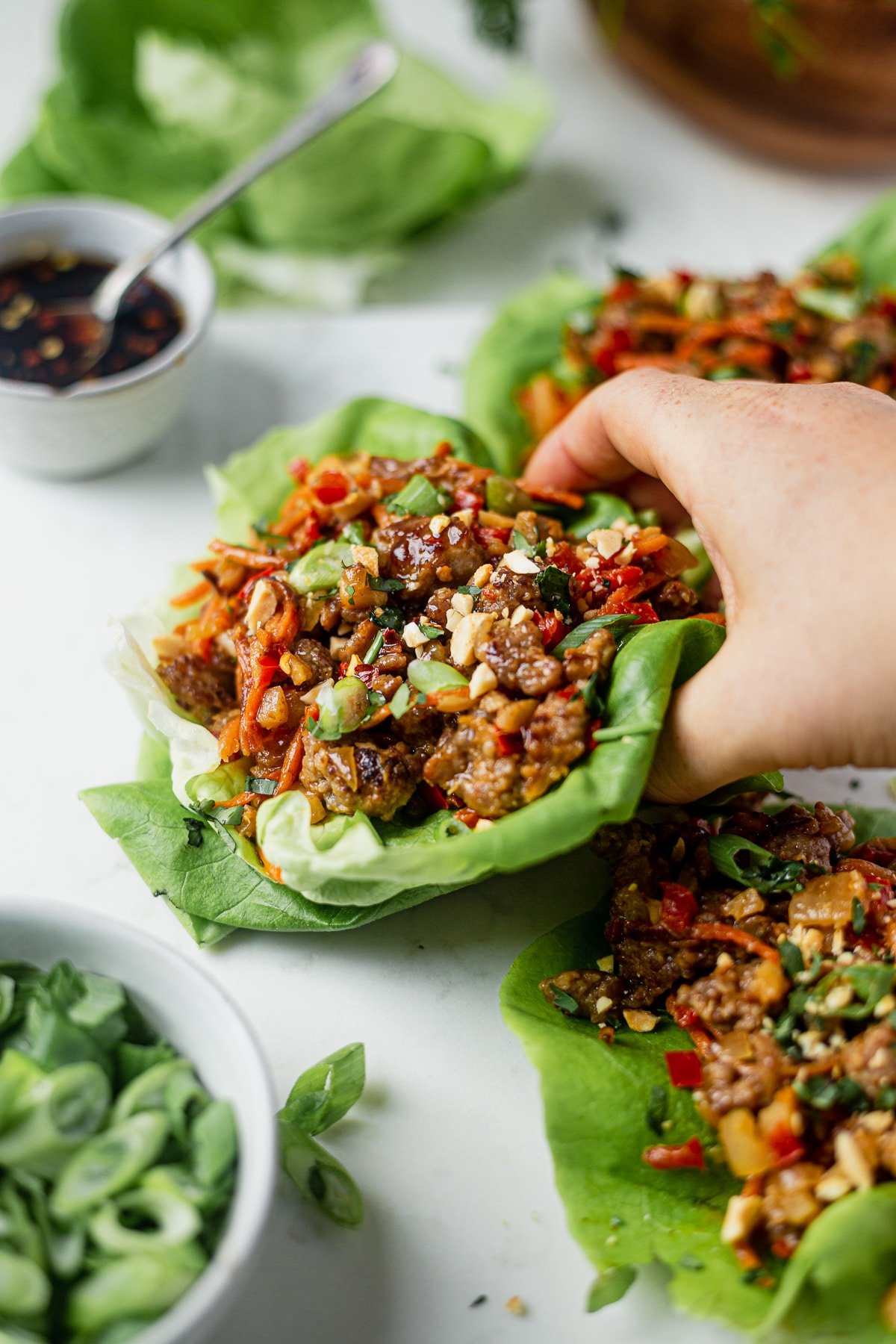 a woman picking up a pork lettuce wrap topped with cilantro and peanuts