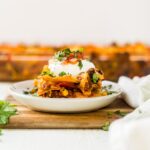 layers of mexican lasagna on a white plate topped with sour cream, salsa and cilantro